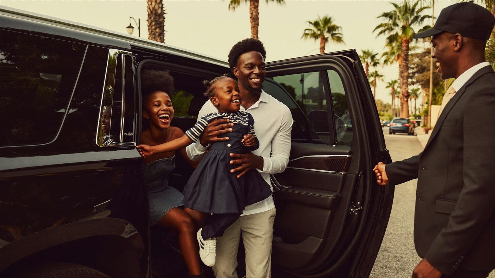 A family stepping out of a black SUV as their chauffeur holds the door